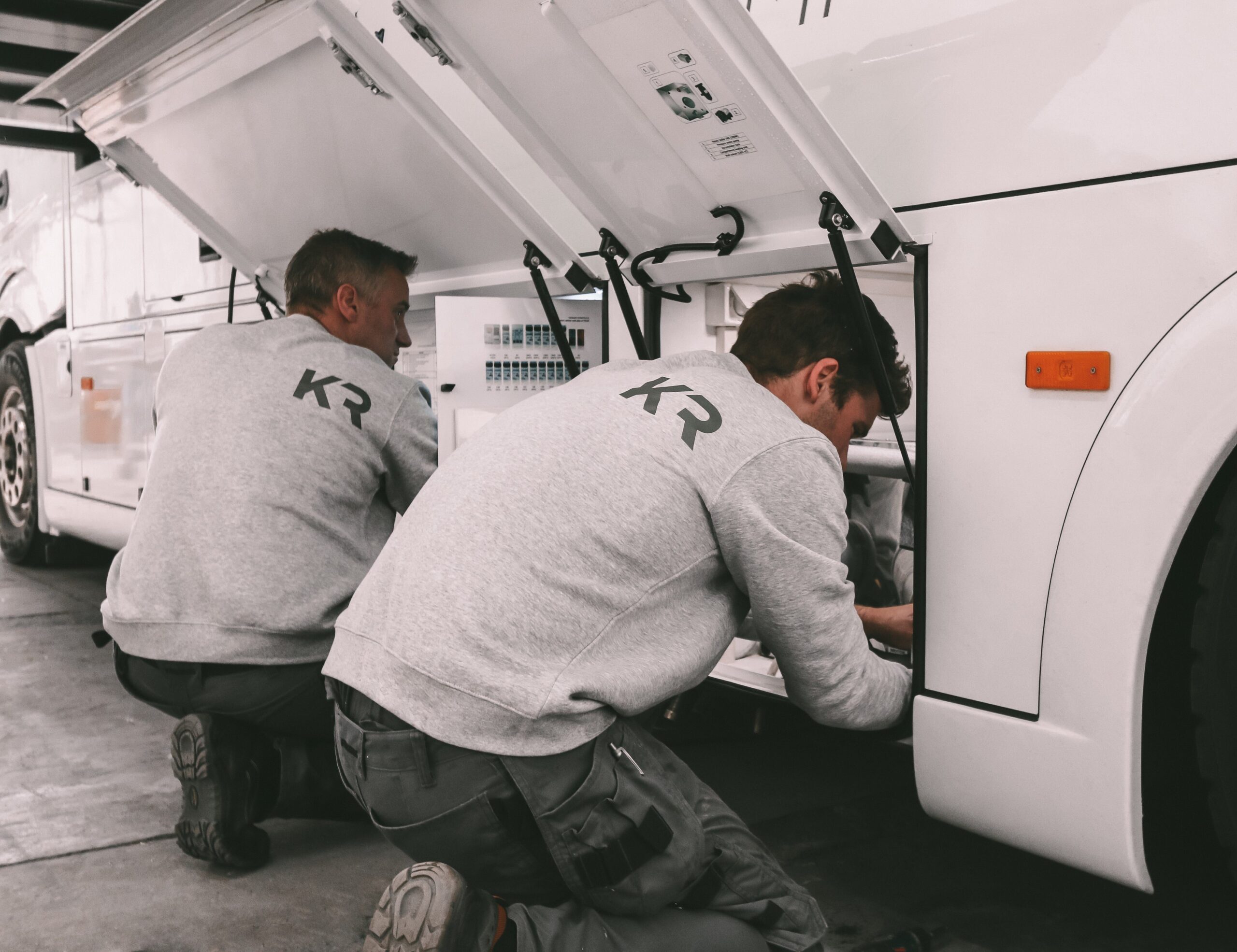 Two technicians on there knees working on a Krismar horse truck wearing both a Krismar sweater